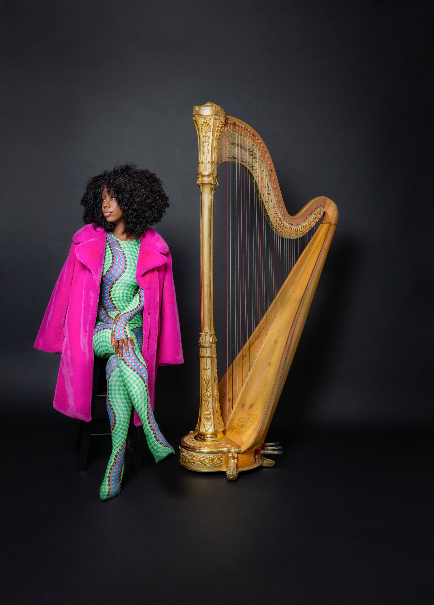 Brandee Younger in a pink coat beside a gilded harp